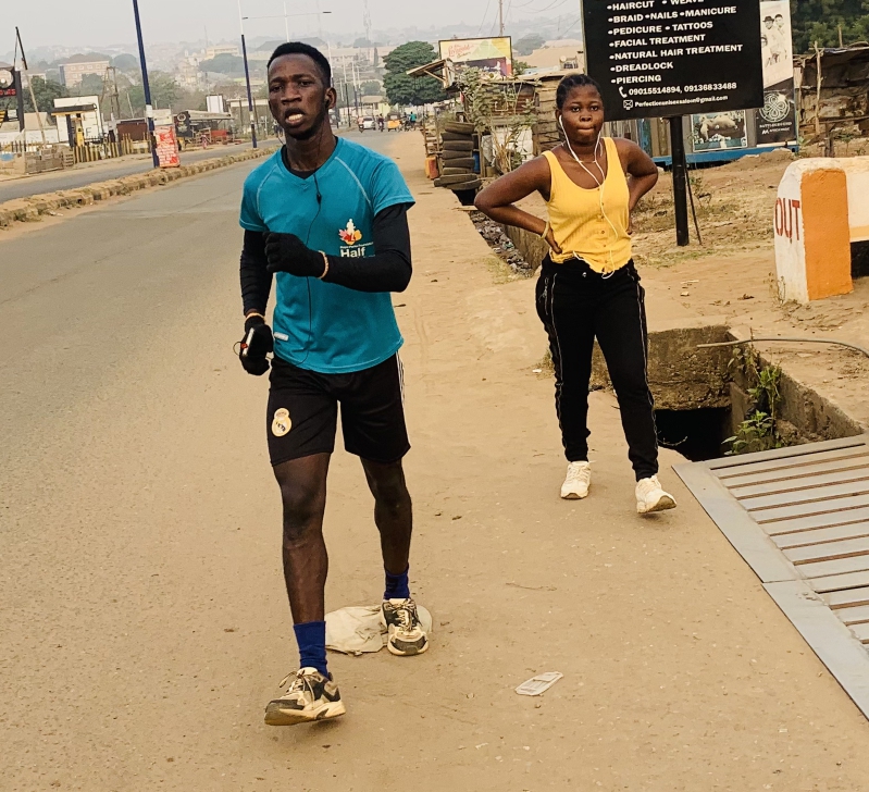 길가에서 조깅을 하는 남성과 뒤에서 쉬고 있는 여성